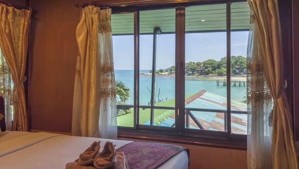 A hotel room with a bed, a view of a beach, and a wooden deck. - Tongta Phaview (Rayong)