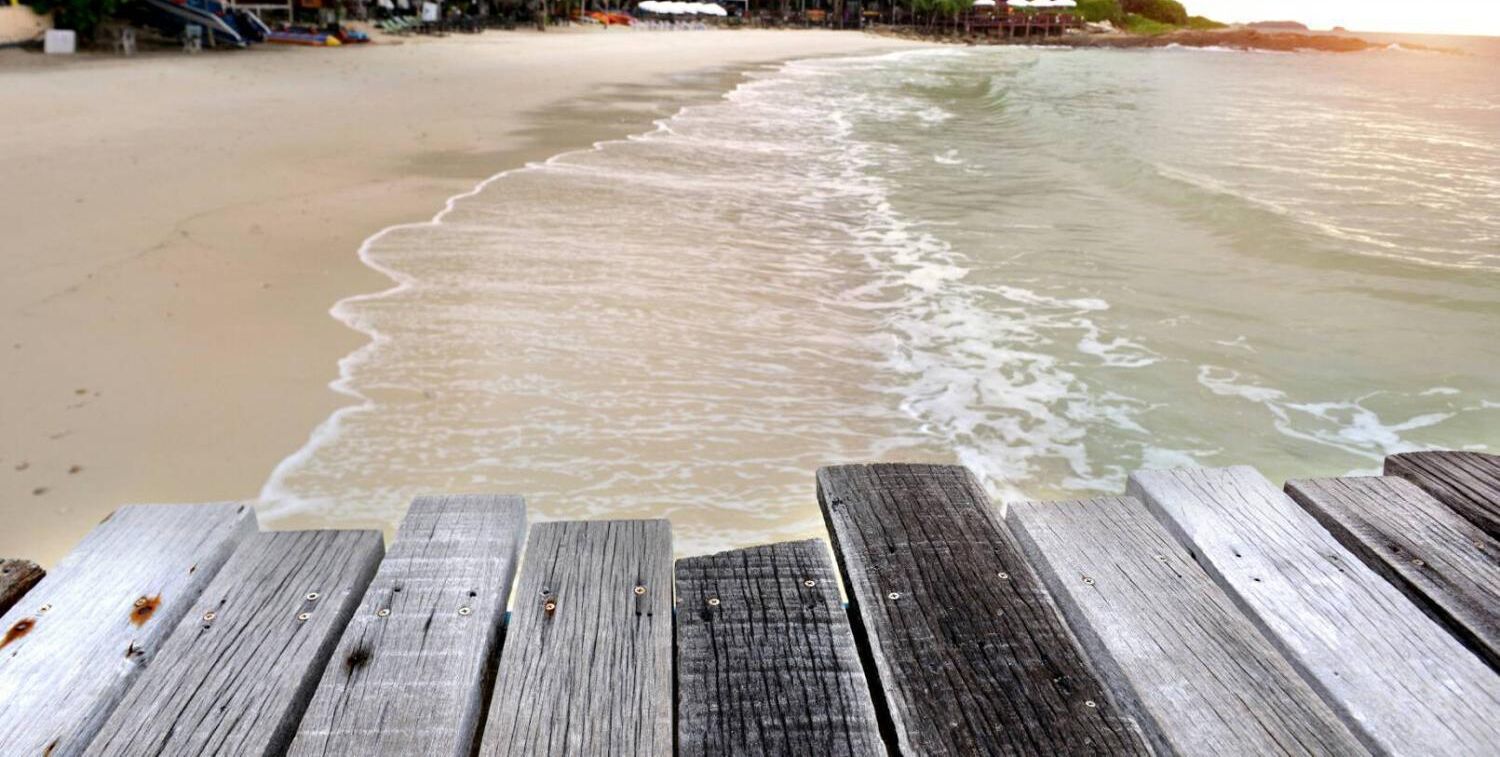 A wooden deck overlooking a beach with waves approaching the shore.