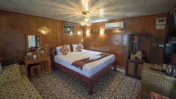 A hotel room with a wooden bed, a nightstand, a mirror, an air conditioning unit, a ceiling fan, and a small table with snacks.