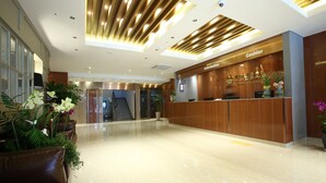 Ein Hotel-Rezeptionsbereich mit einem Holzbüro, einer Kasse und einer Treppe im Hintergrund.