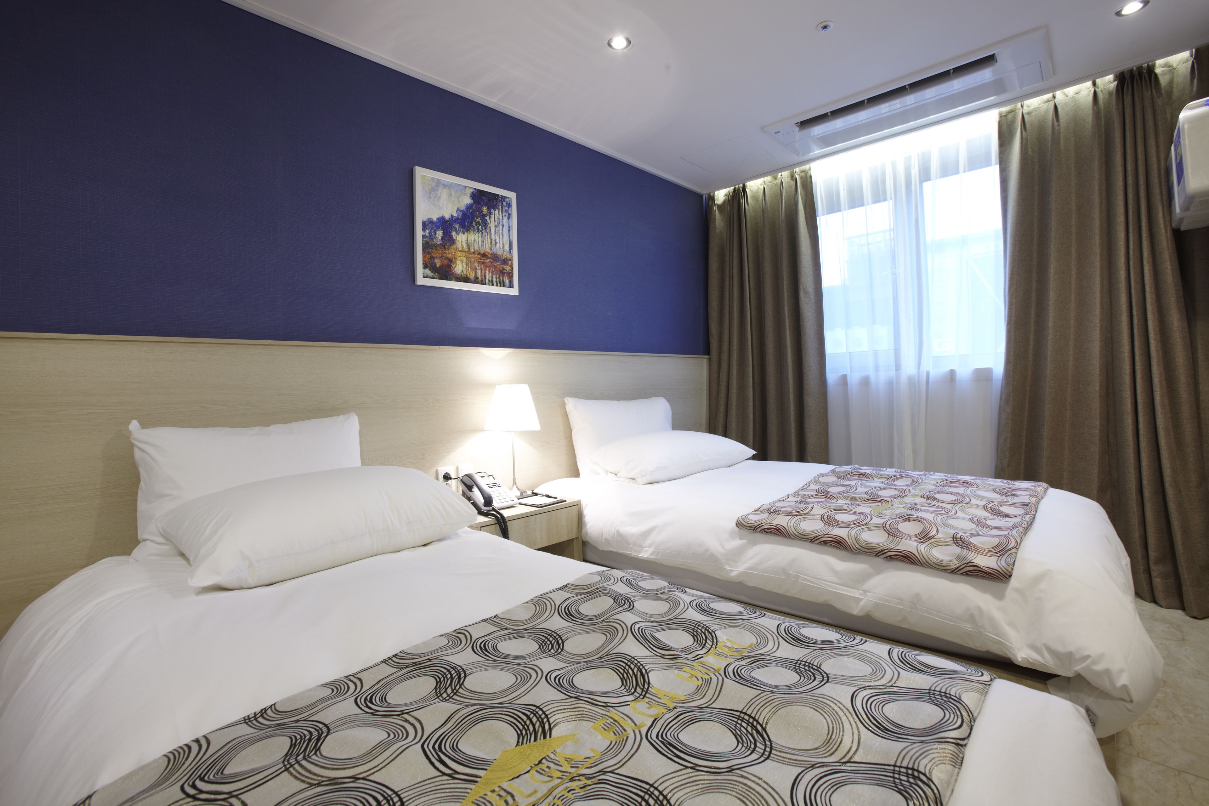 A hotel room with two beds, a painting on the wall, and a window with curtains.