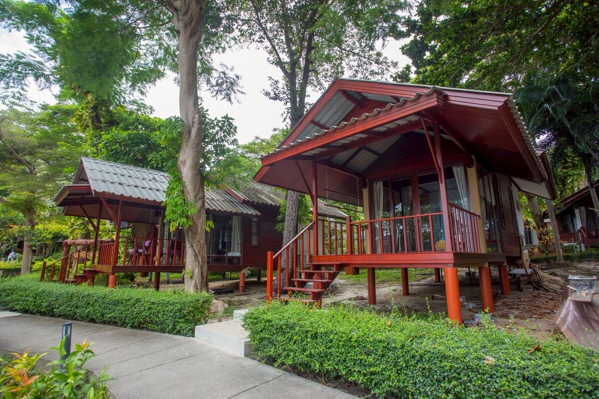 A wooden cabin with a porch and staircase, surrounded by lush greenery and trees.