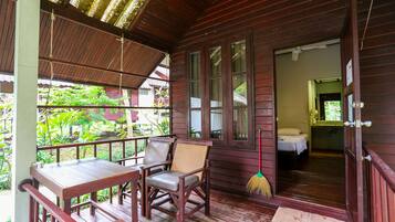 A wooden cabin with a porch, a dining table with chairs, and a bedroom visible through an open door.