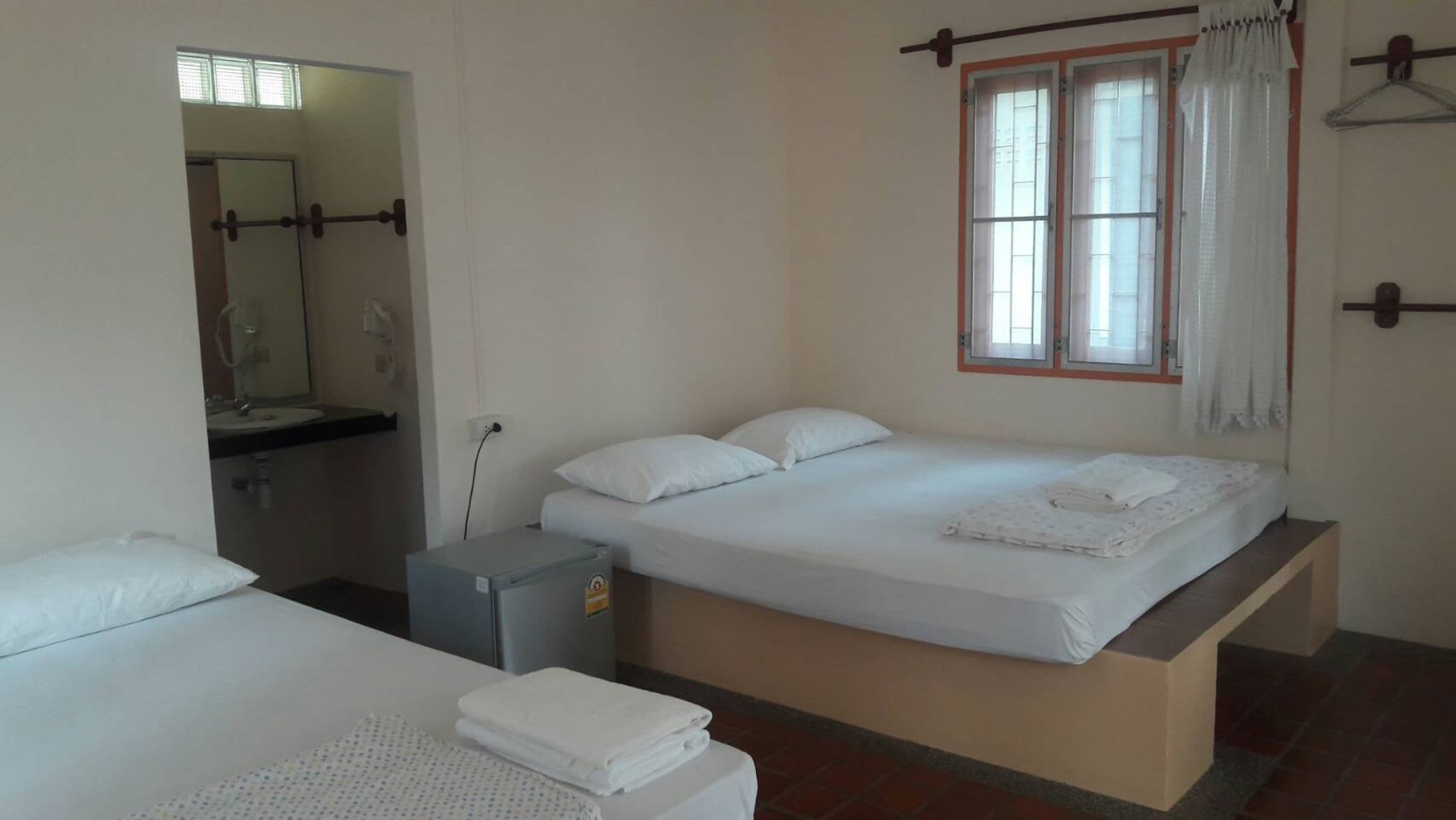 A bedroom with a bed, a small desk, a mirror, and a window with curtains.
