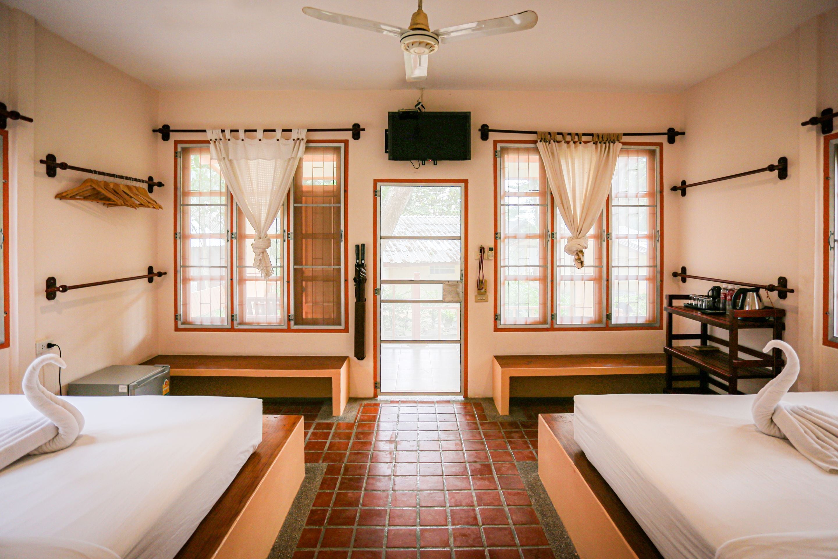 A hotel room with two beds, a TV, a wooden bench, and a tiled floor.