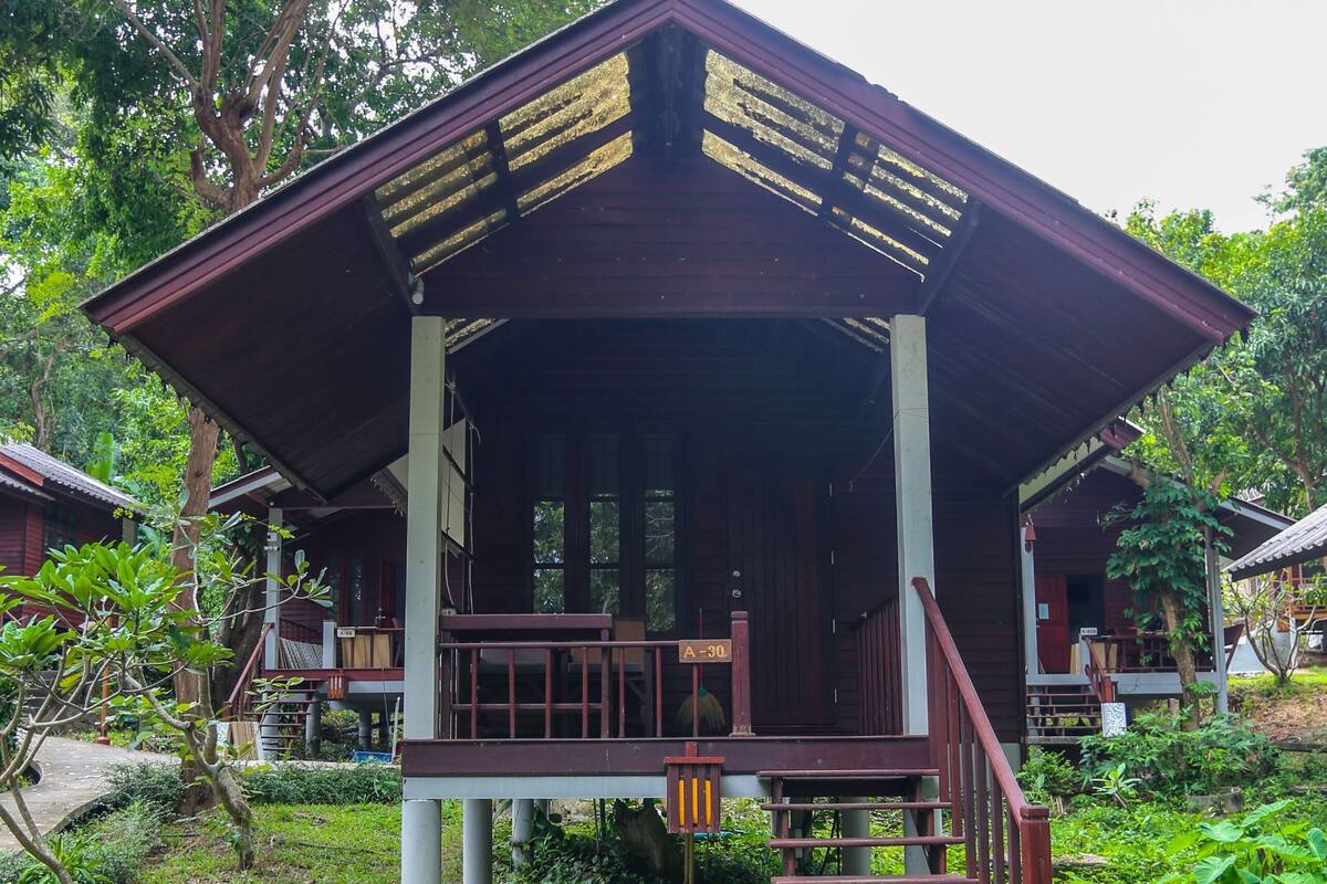 A wooden structure with a porch and steps leading up to it, surrounded by greenery.