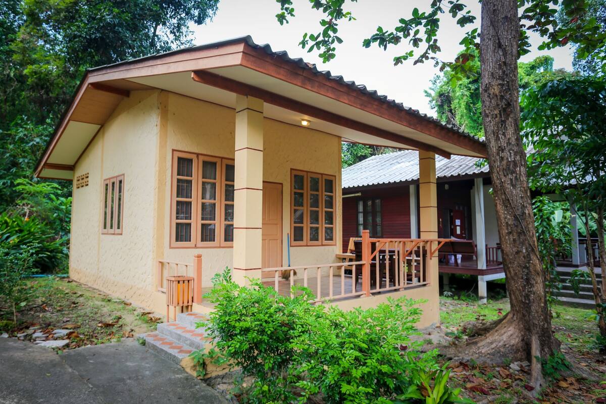 A two-story house with a porch, surrounded by greenery.