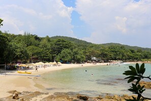 Una playa con agua cristalina, una orilla arenosa y una colina boscosa al fondo.