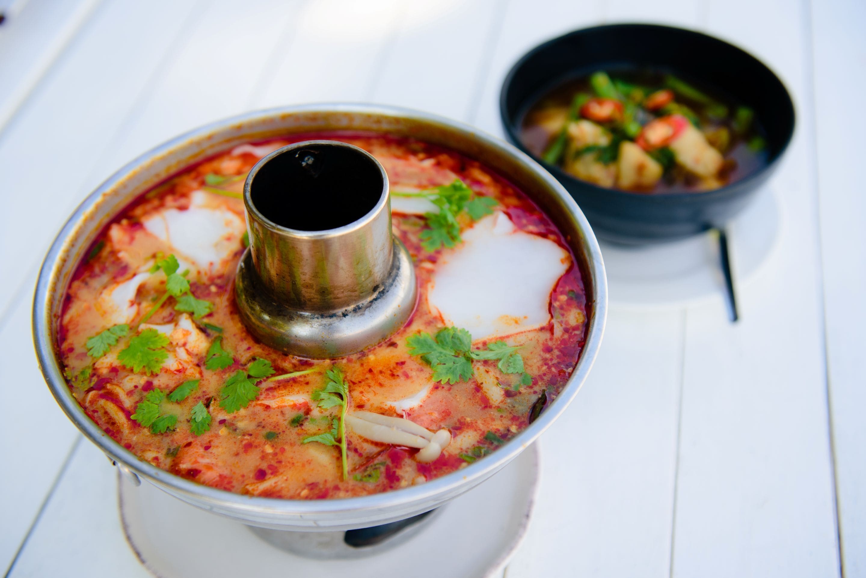 A large pot of soup with a ladle, garnished with herbs, on a white surface.