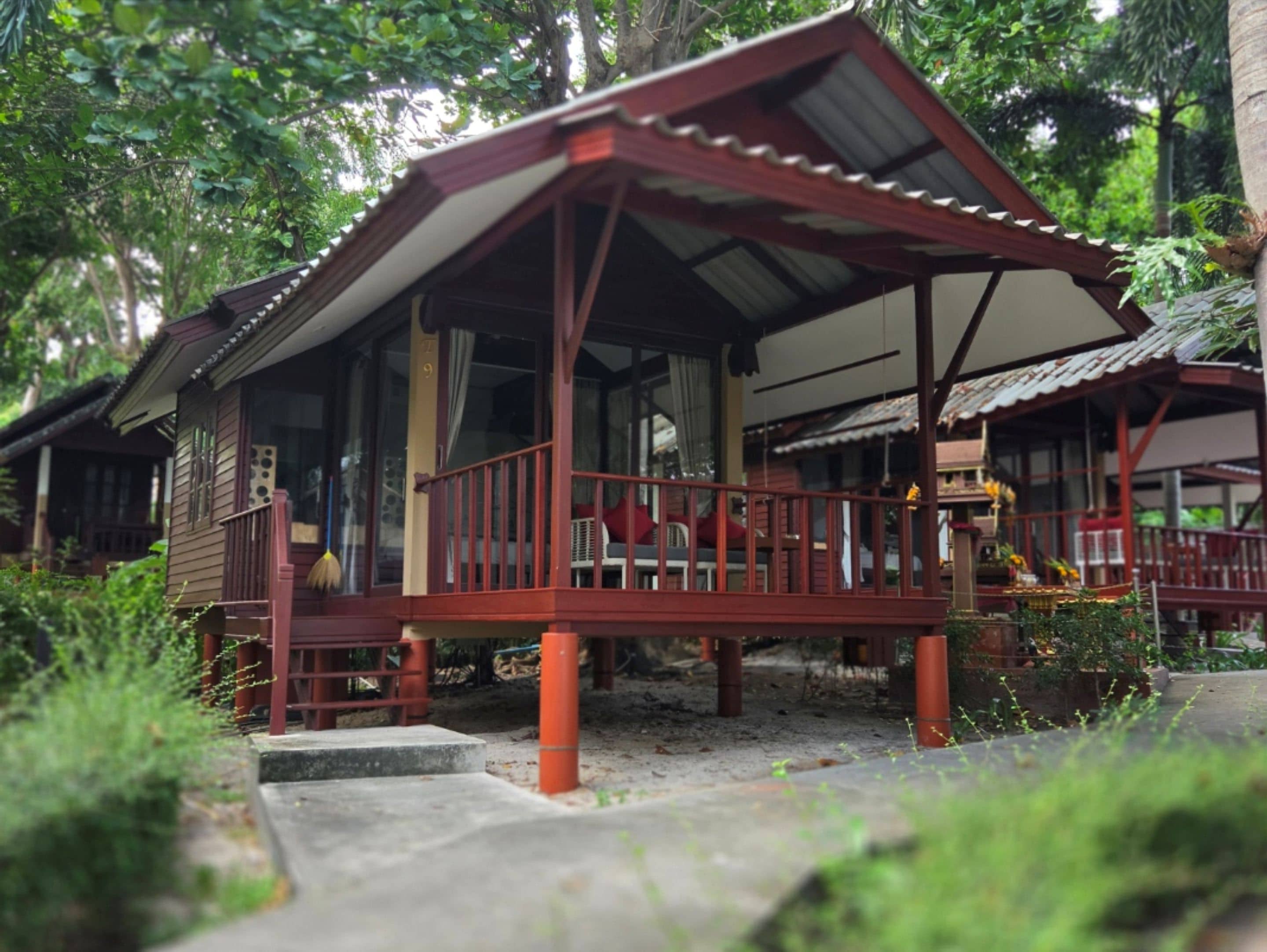 A wooden structure with a porch and a covered area, surrounded by greenery.