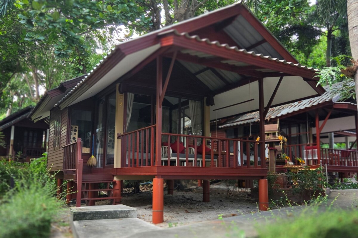 A wooden structure with a porch and a covered area, surrounded by greenery.