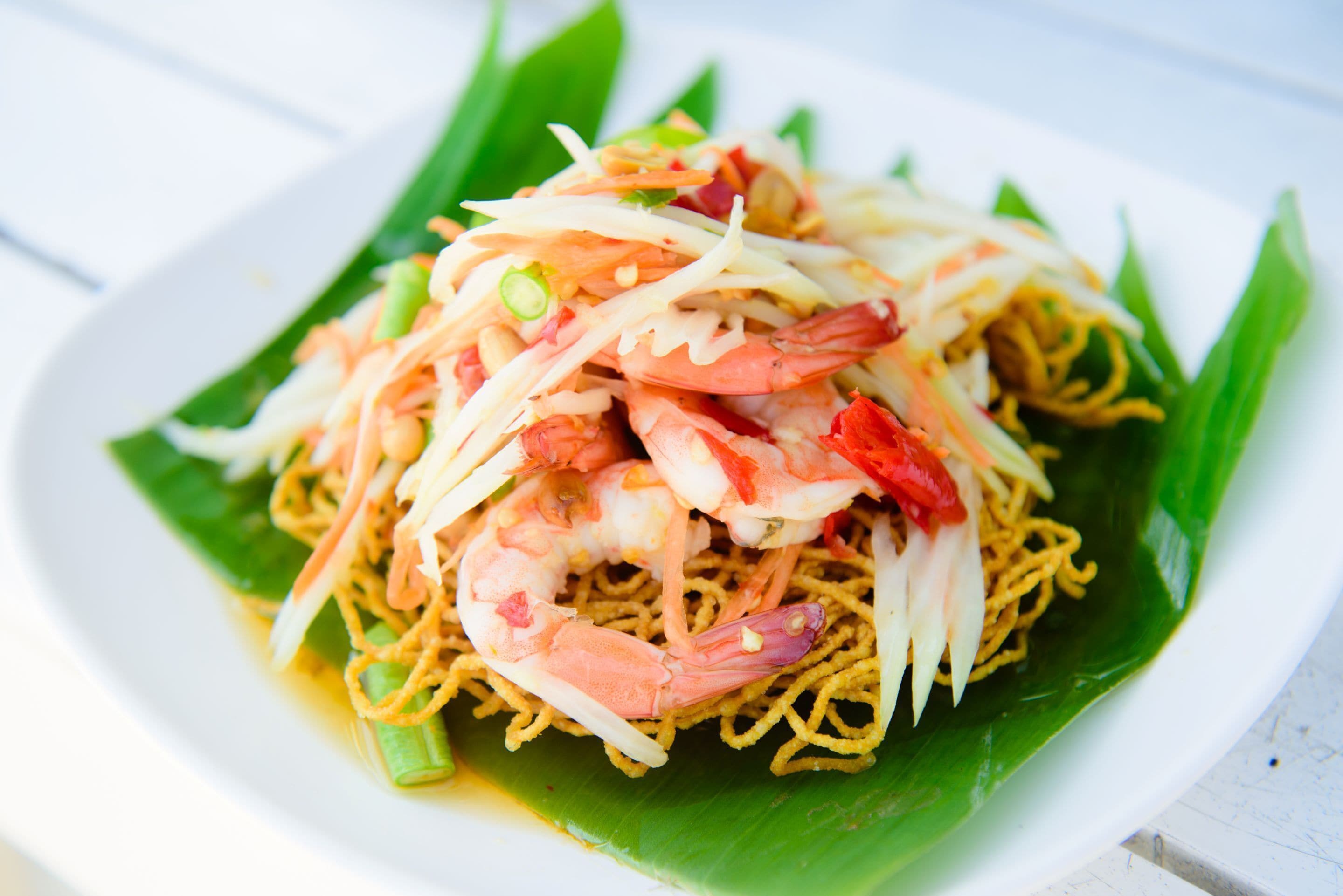 A plate of noodles with shrimp and vegetables on a green leaf.