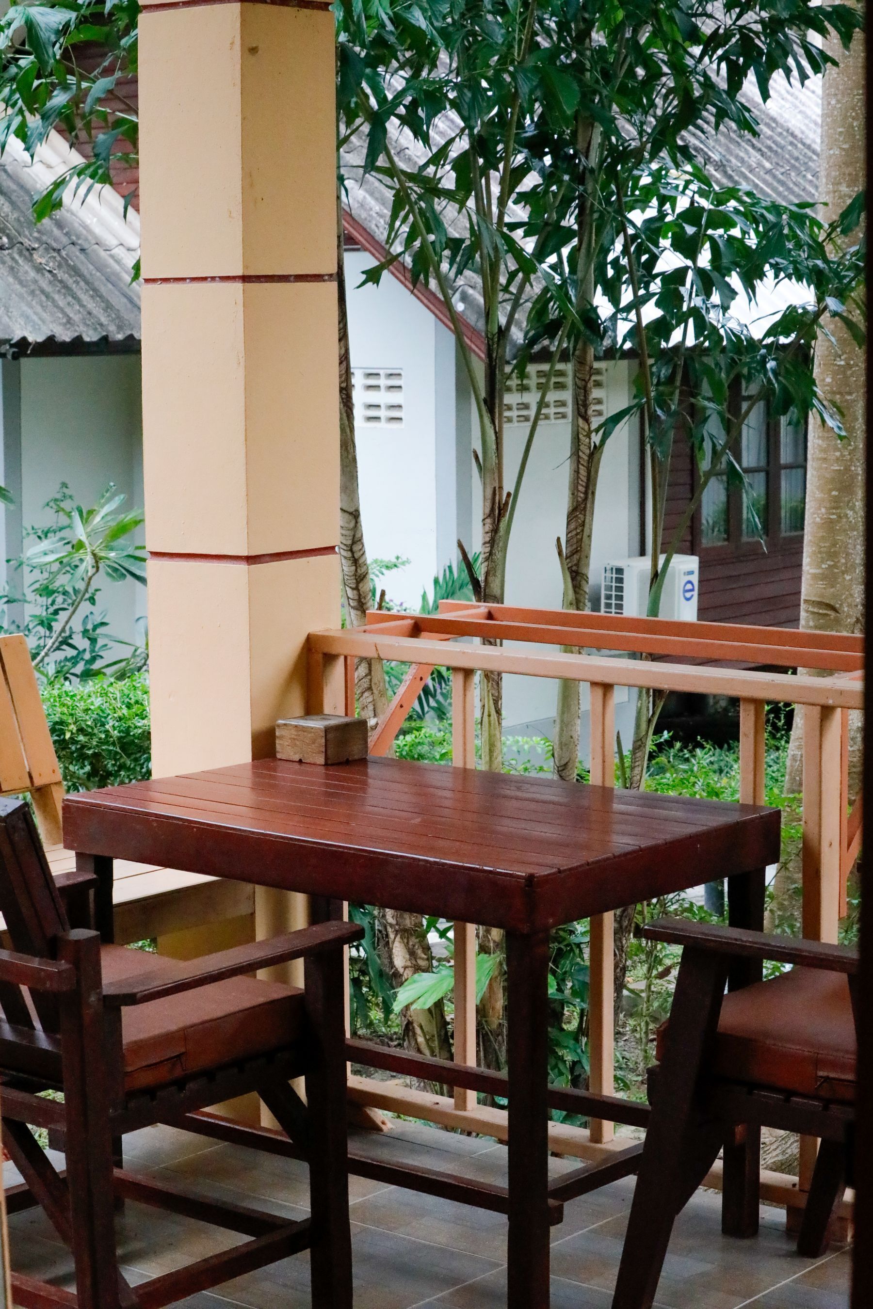 A wooden table and chairs set outdoors with a view of a building and greenery.