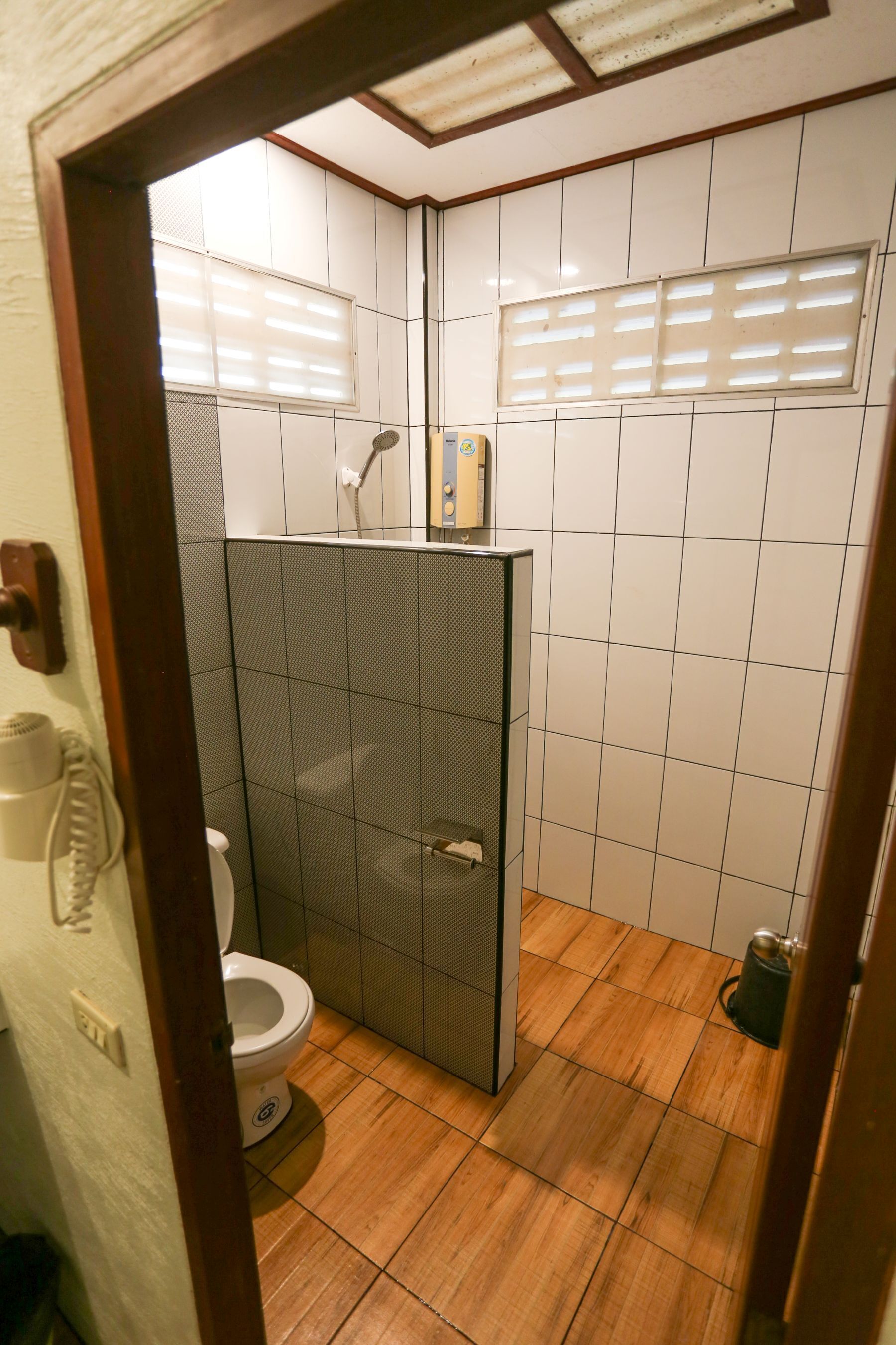 Un bany petit amb rajoles, amb vàter, dutxa i un lavabo.