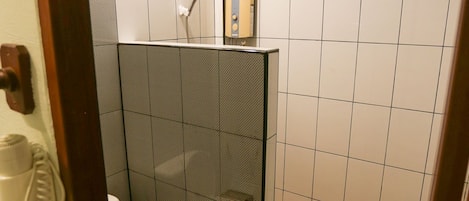 Un bany petit amb rajoles, amb vàter, dutxa i un lavabo.