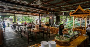 An outdoor restaurant with wooden tables and benches, a buffet area with food dishes, and a bar counter. - Tubtim Resort (Rayong)