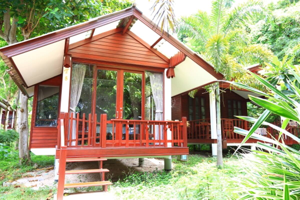 A wooden cabin with a balcony, surrounded by lush greenery.