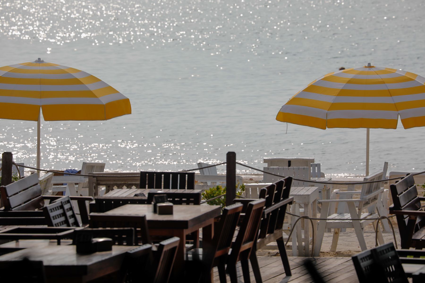 Un restaurante frente al mar con mesas al aire libre y dos sombrillas a rayas amarillas.