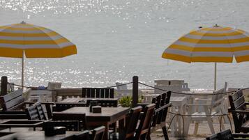 Un restaurante frente al mar con mesas al aire libre y dos sombrillas a rayas amarillas.