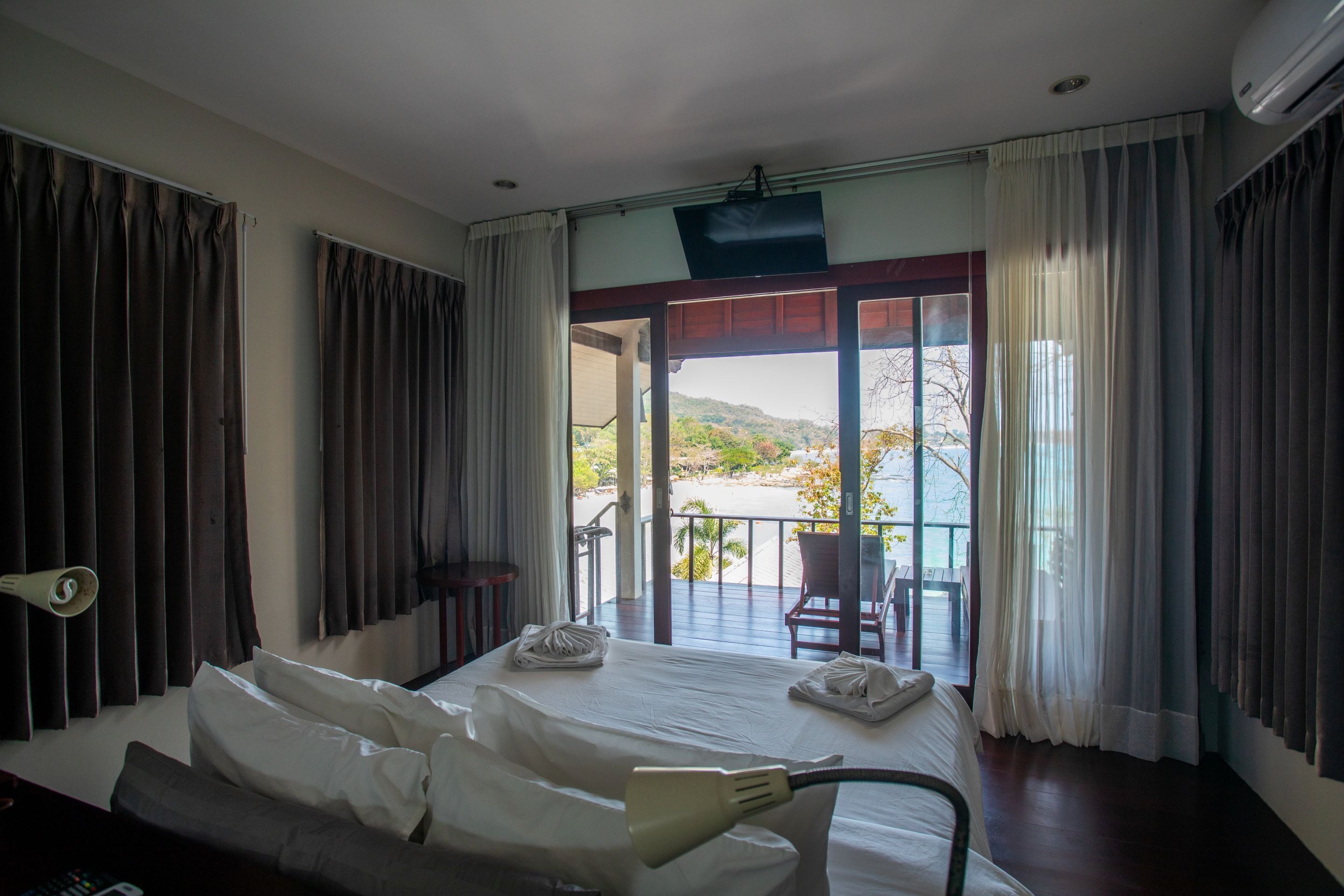 A hotel room with a bed, a TV, and a balcony with a view of the sea.