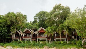 A row of wooden cabins with balconies, surrounded by lush greenery and trees. - Tubtim Resort (Rayong)