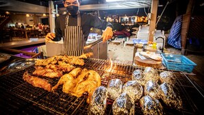A person grilling food outdoors with a grill and foil-wrapped items. - Tubtim Resort (Rayong)