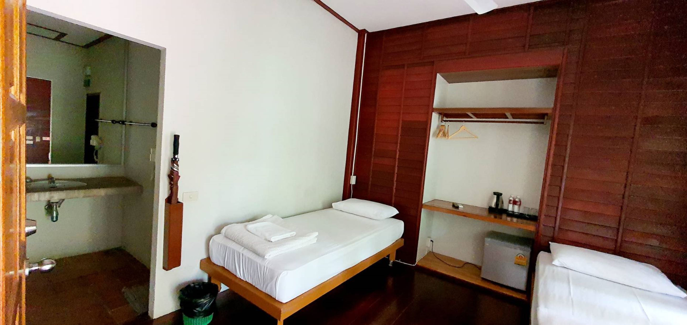 A small, compact room with a single bed, a wooden wardrobe, a small sink, and a mirror.
