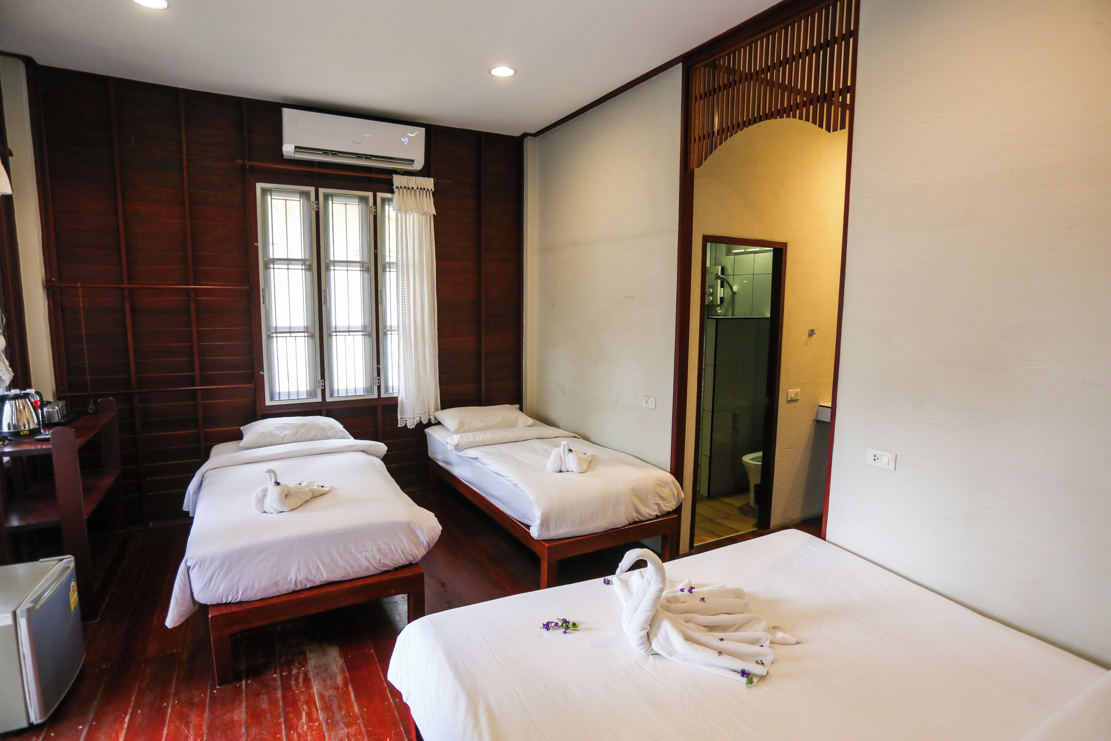 A hotel room with two single beds, a small table with a kettle, and a shower area.