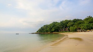A beach with a sandy shore, a calm sea, and a forested hill with buildings. - Tubtim Resort (Rayong)