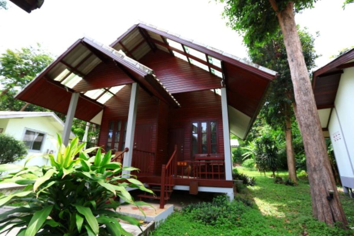A wooden structure with a sloped roof and a porch, surrounded by greenery.