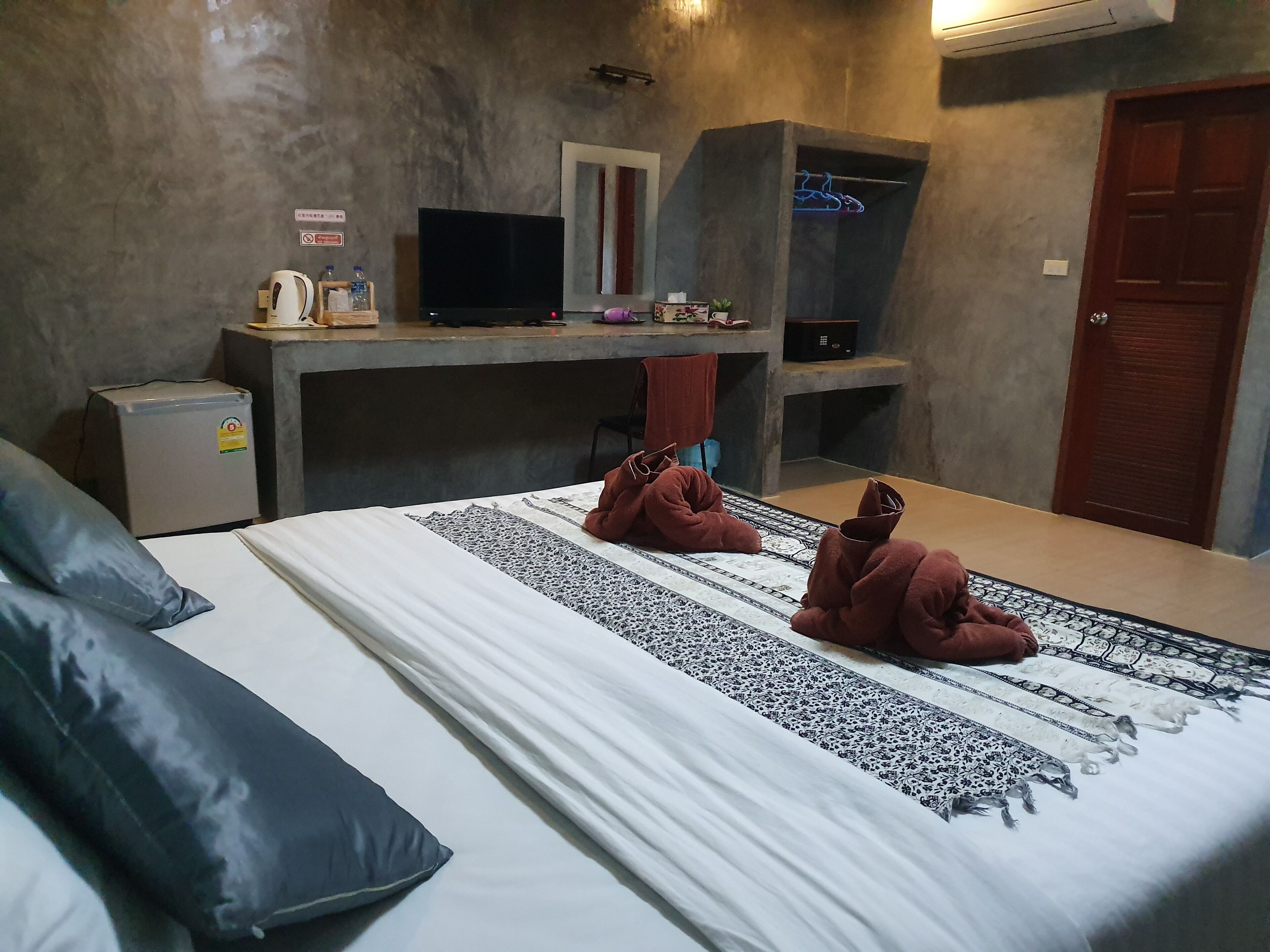 Hotellihuone, jossa on sänky, työpöytä, televisio, pieni jääkaappi ja vaatekaappi.