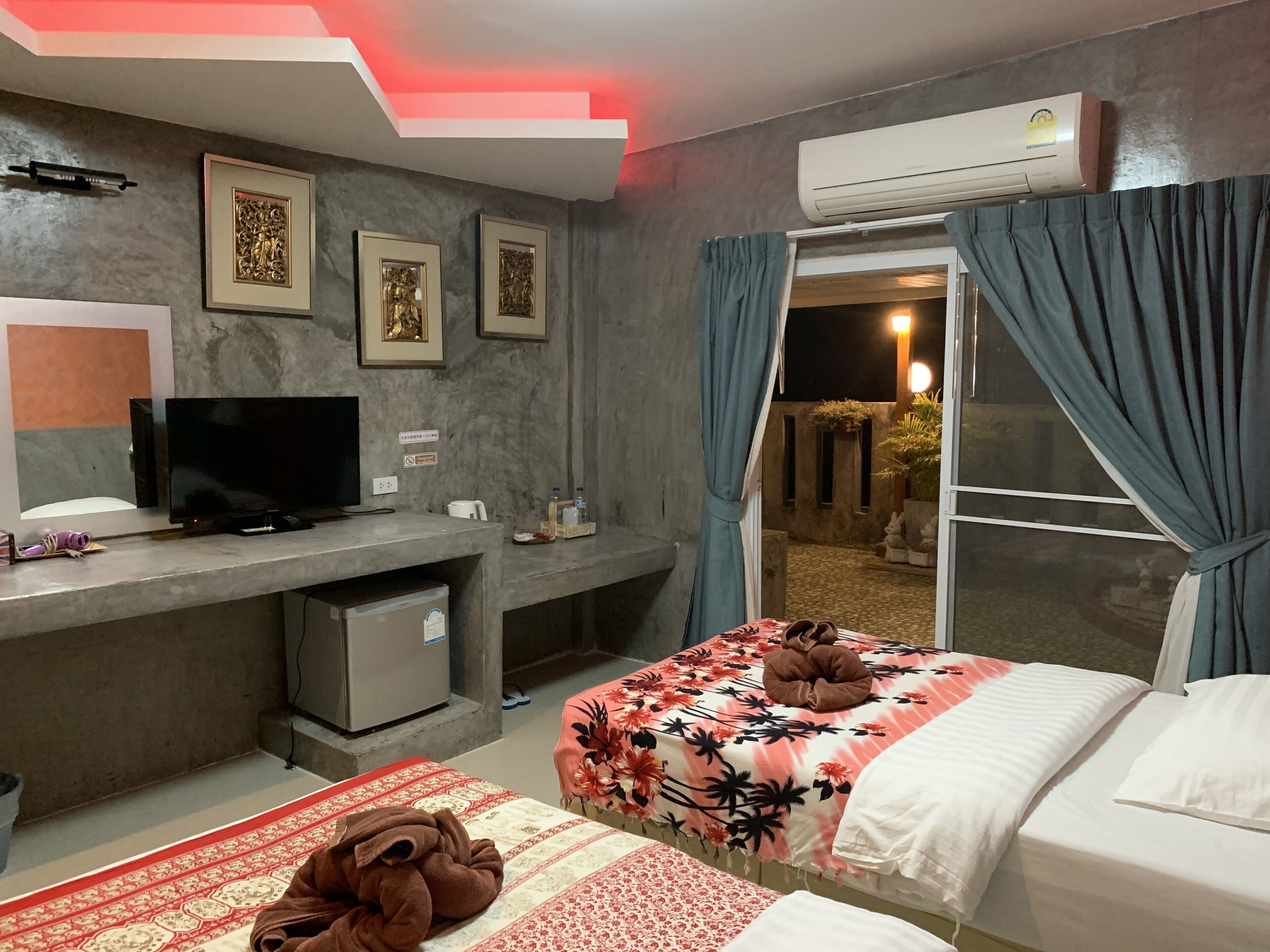 A hotel room with a bed, a desk with a television, a small fridge, and a window with curtains.