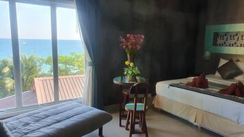 Un dormitorio con cama, una silla, una mesita con un florero y vistas al océano.