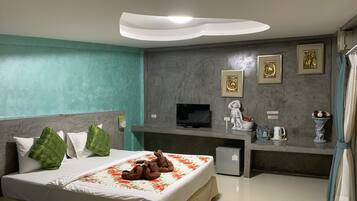 A hotel room with a bed, a TV, a small fridge, a decorative statue, and a flower vase.