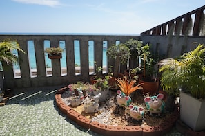 A rooftop garden with potted plants, decorative rabbit and pig sculptures, and a view of the sea.