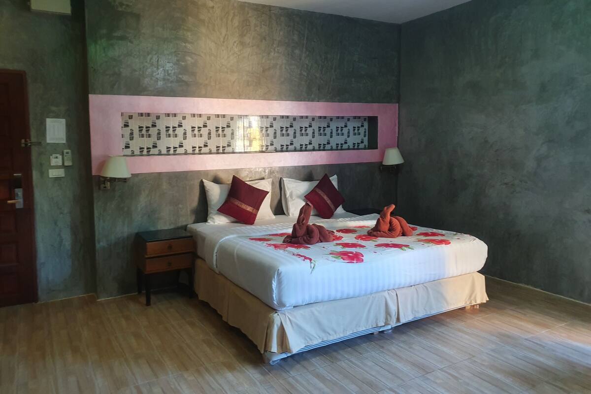 A hotel room with a large bed, a nightstand, a lamp, and a wall with a decorative panel.