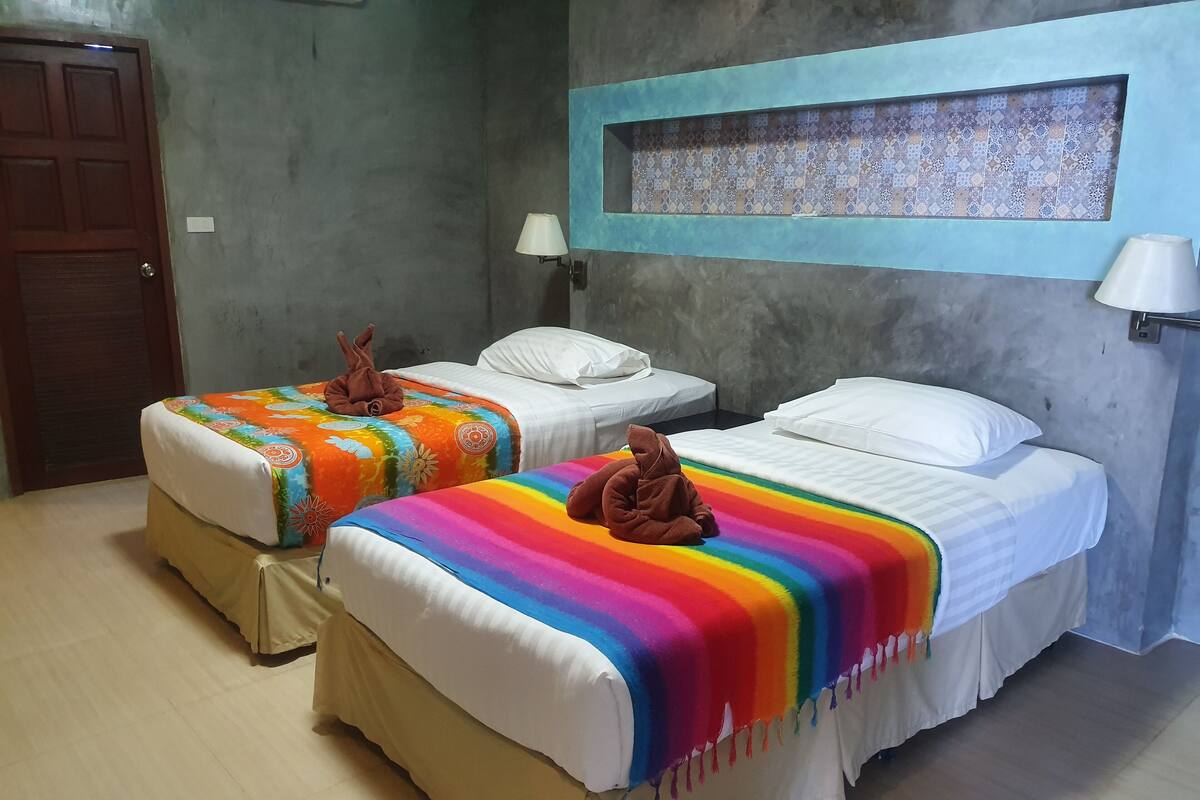 A hotel room with two beds, each with a colorful blanket and a brown towel. There is a wall-mounted shelf with decorative tiles above the beds.