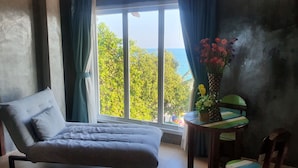 Ein Zimmer mit einem Bett, einem Sessel, einem kleinen Tisch mit Blumen und Meerblick durch ein großes Fenster.
