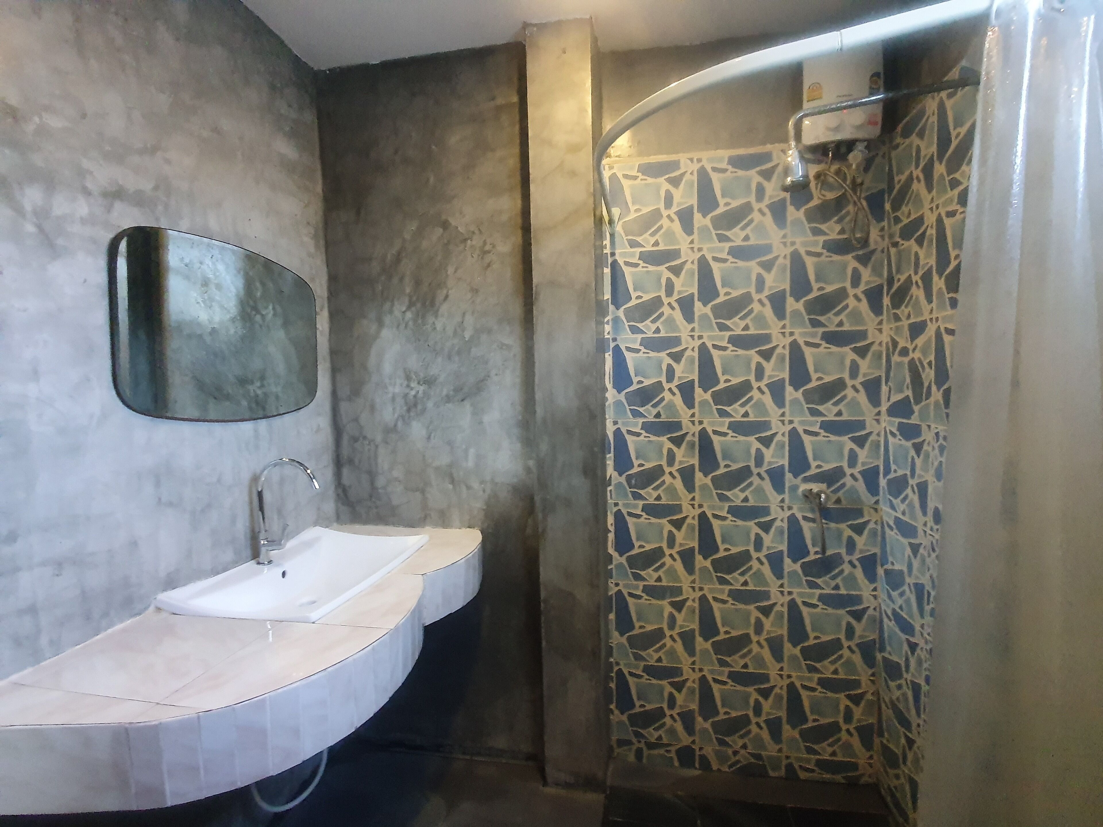 Een badkamer met een gebogen douche, een wastafel met spiegel en een wand betegeld met mozaïek.