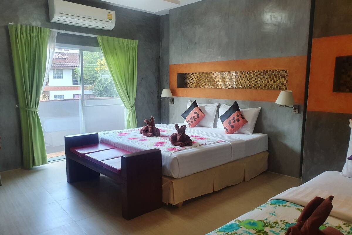 A hotel room with a bed, a small table, a window with curtains, and an air conditioning unit.