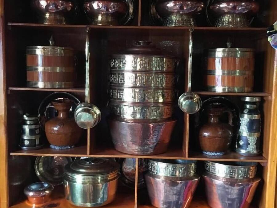 A wooden cabinet with multiple shelves holding various metal containers and pottery.