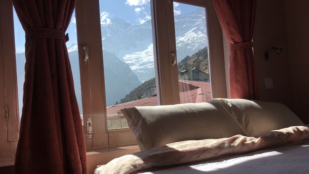Une chambre à coucher avec un lit, des rideaux et une fenêtre donnant sur la montagne.