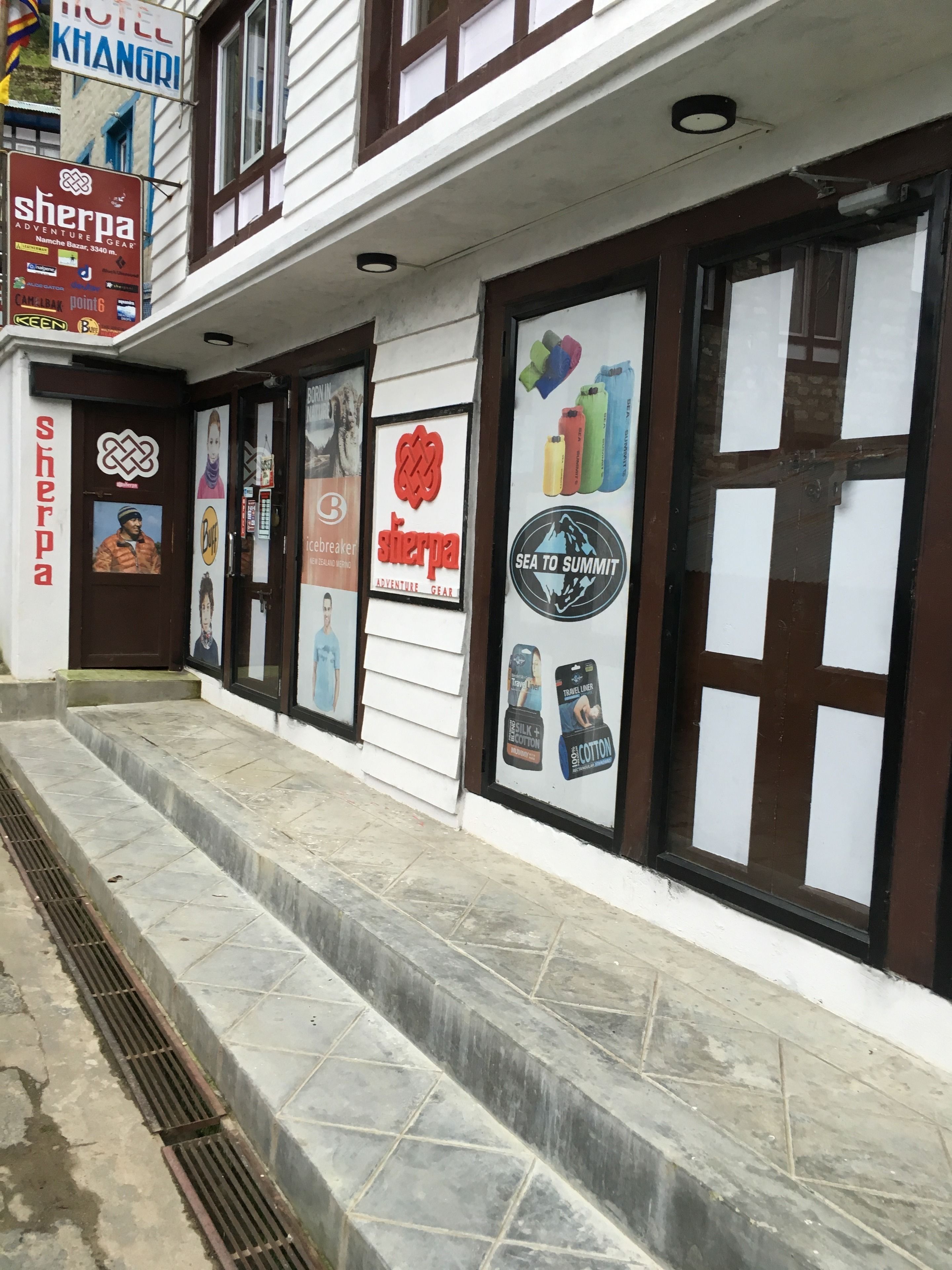 A hotel facade with multiple signs, including 'Sherpa Adventure Gear' and 'Hotel Khanori'.