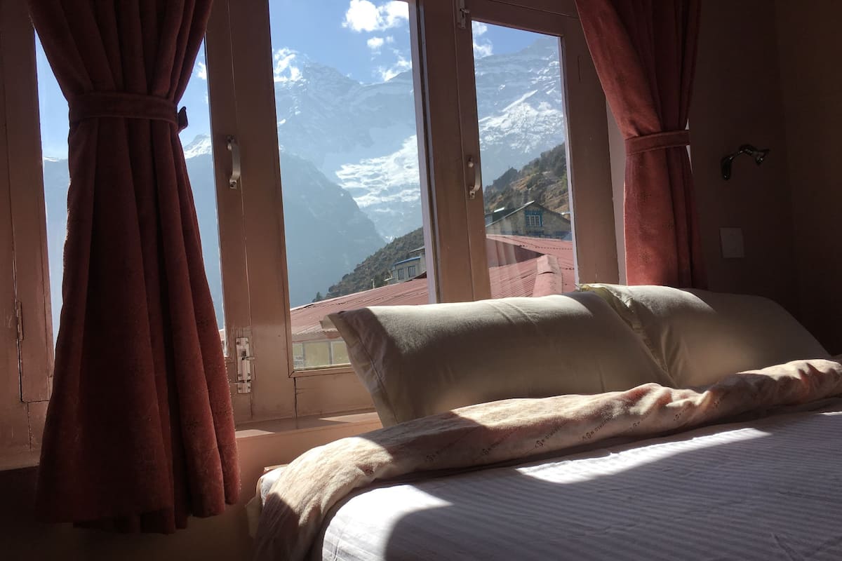 Ein Schlafzimmer mit Bett, Vorhängen und einem Fenster mit Blick auf die Berge.