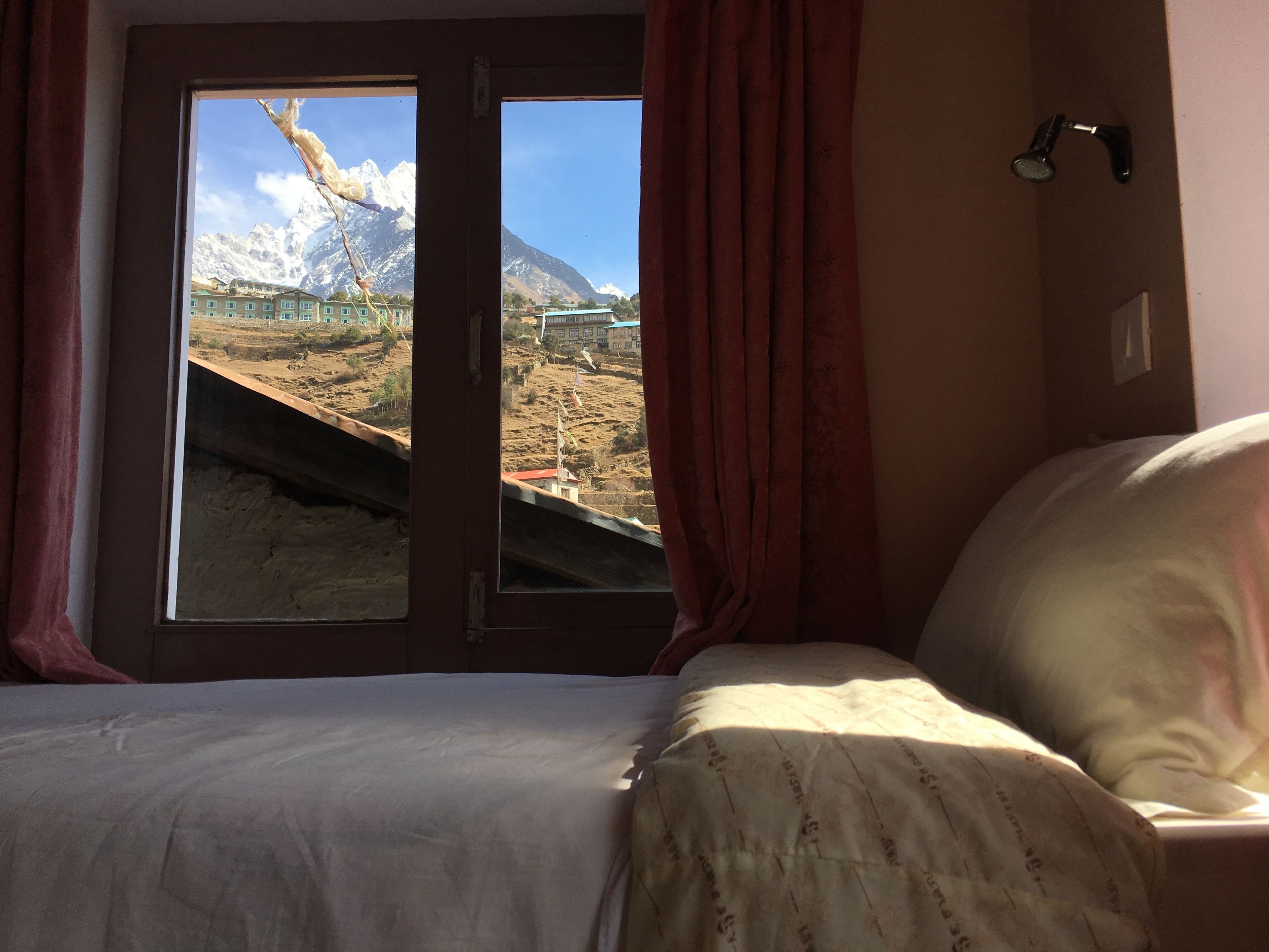 A hotel room with a bed, a window with curtains, and a view of a mountainous landscape.