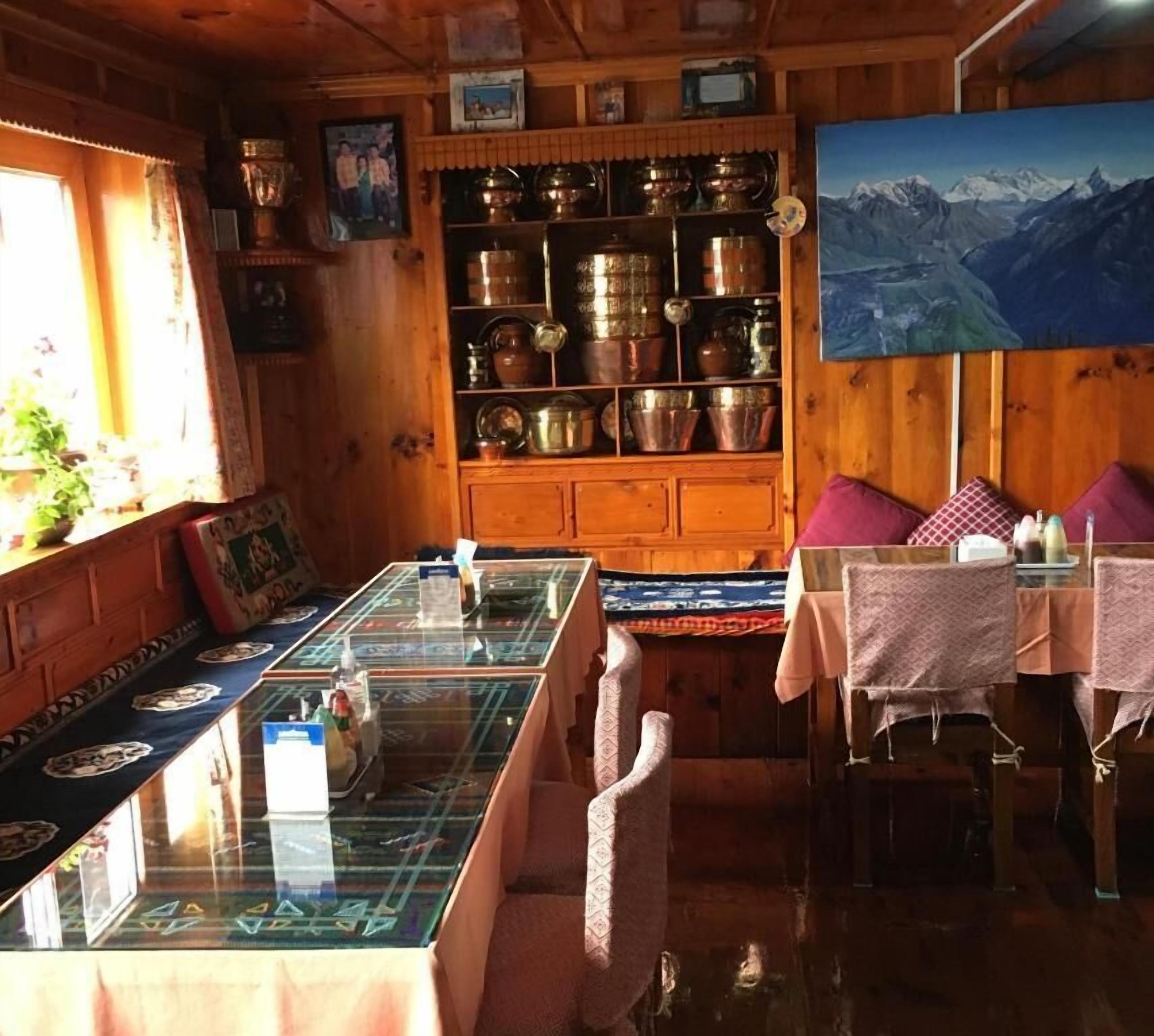 A wooden interior with a dining area featuring a glass-top table, chairs, and a painting of mountains.