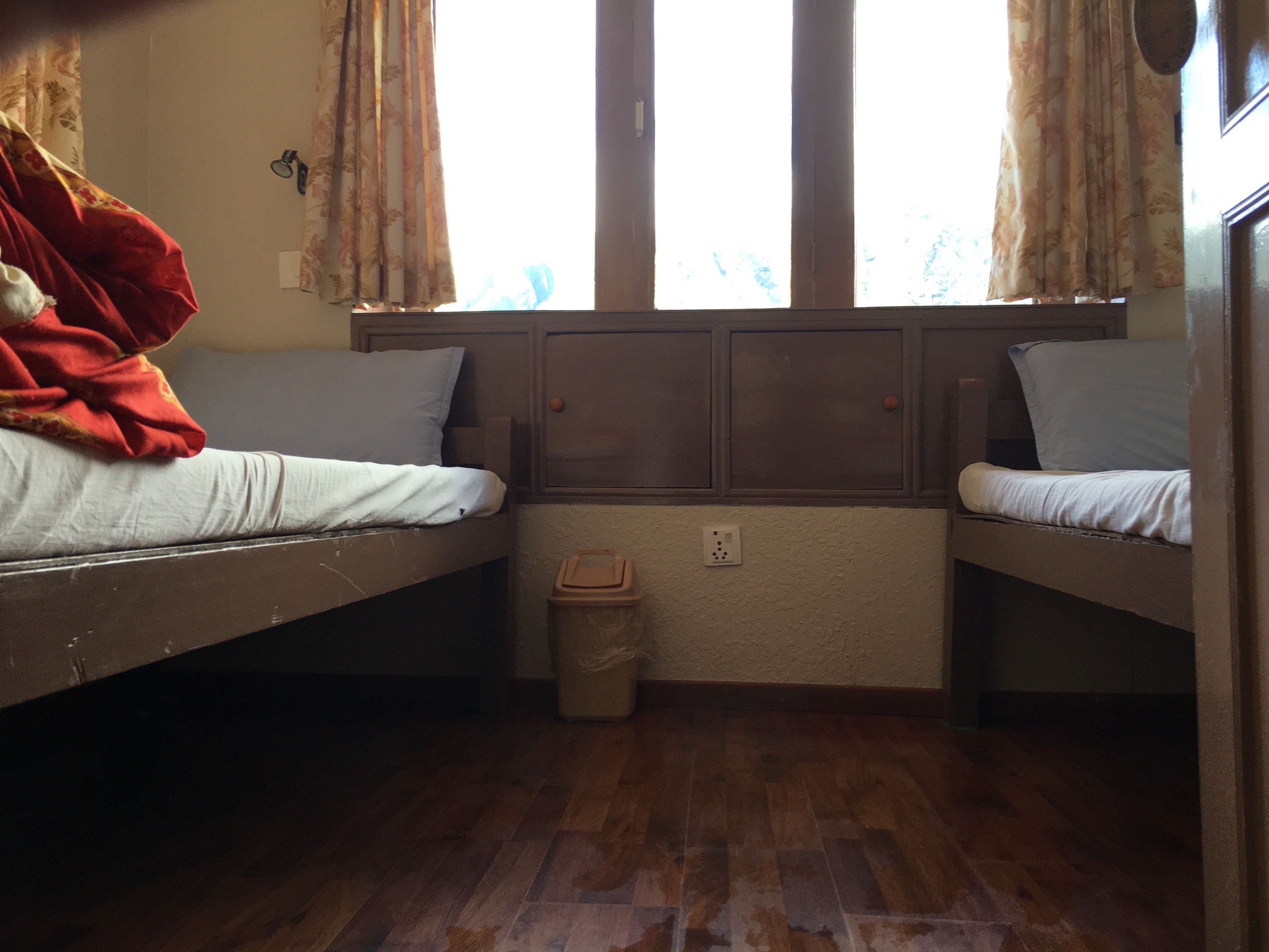 Habitación tipo dormitorio con dos literas, suelo de madera, un cubo de basura pequeño y una ventana con cortinas.