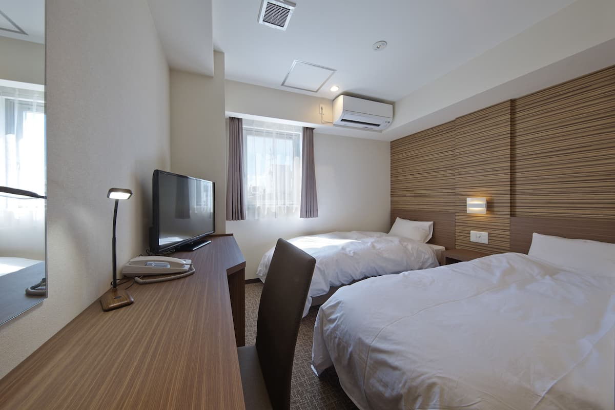 Une chambre d’hôtel avec deux lits, un bureau avec une télévision, une chaise, une lampe de bureau et un appareil de climatisation.