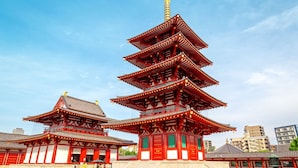 Une pagode traditionnelle à plusieurs niveaux, aux couleurs rouge et blanche, entourée de bâtiments modernes.