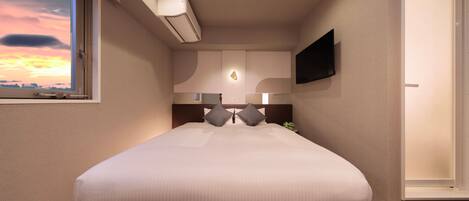Habitación de hotel con una cama grande, un televisor de pantalla plana montado en la pared, una ventana con vista al atardecer y un equipo de aire acondicionado sobre la cama.